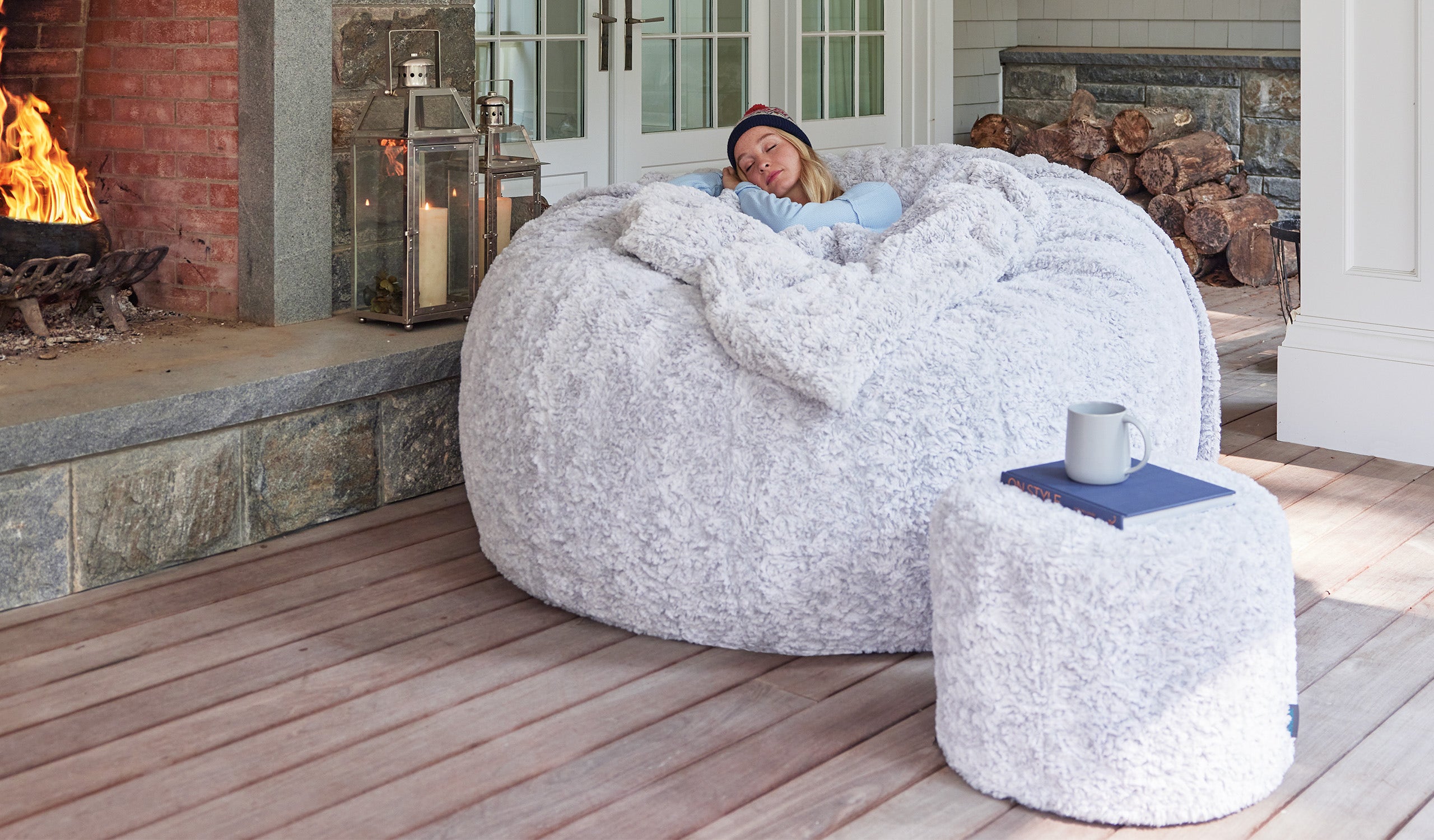 A person relaxing on a large, grey beanbag with a white blanket.
