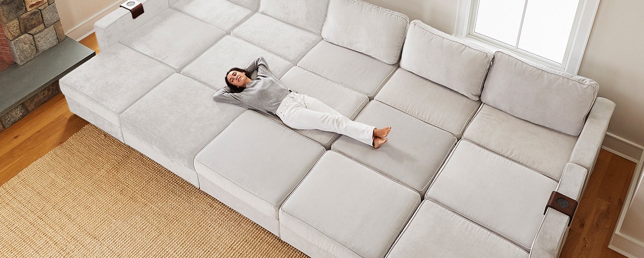 A woman laying down on a large, light-colored Lovesac Sactionals couch.
