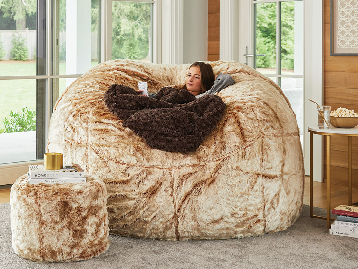 Teen relaxing in a Lovesac BigOne Sac with FootSac while using her phone.